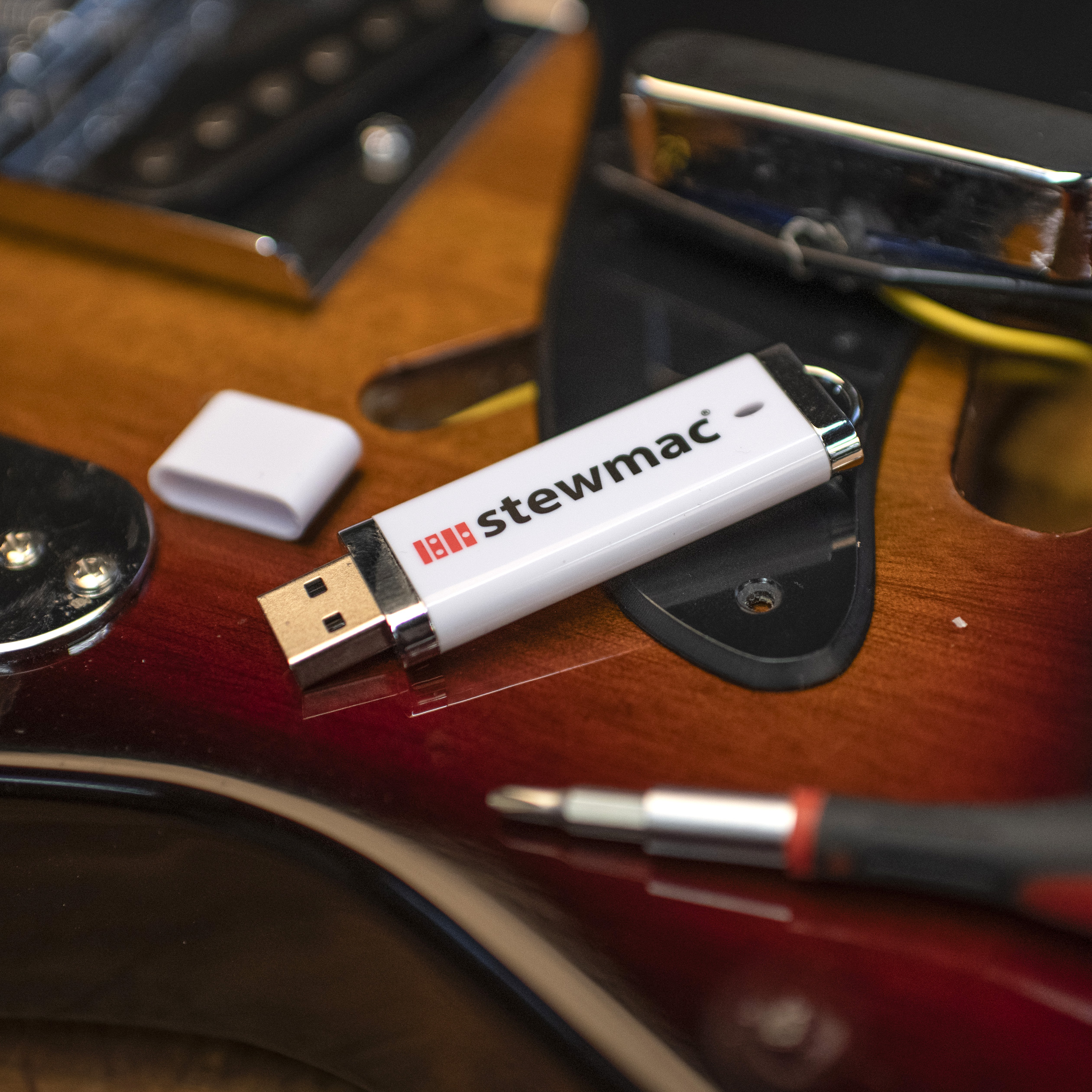 Memoria USB con vídeos de StewMac encima de una guitarra con instrumentos de luthier.