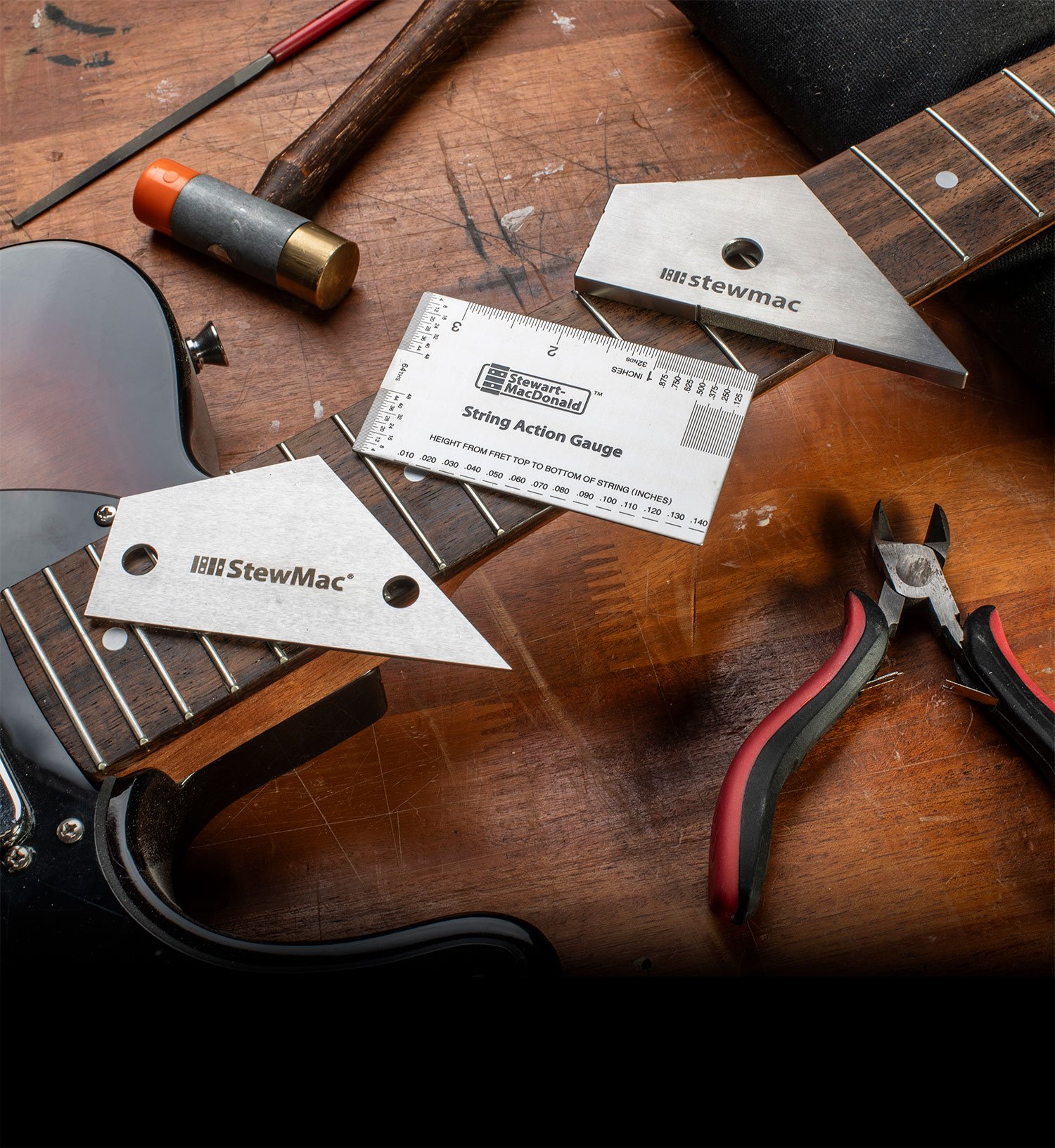 Herramientas de trabajo de trastes esenciales apoyadas sobre un mástil de guitarra en un banco de trabajo.