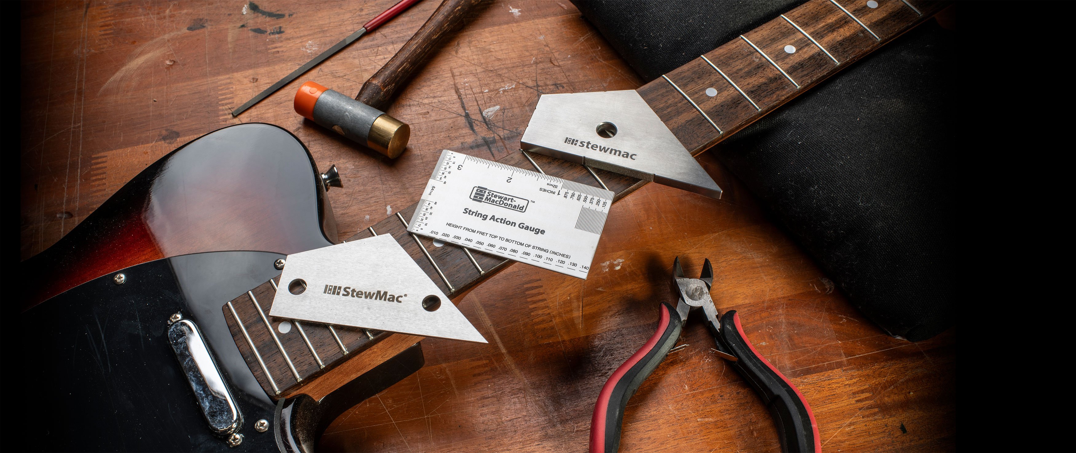 Herramientas de trabajo de trastes esenciales apoyadas sobre un mástil de guitarra en un banco de trabajo.