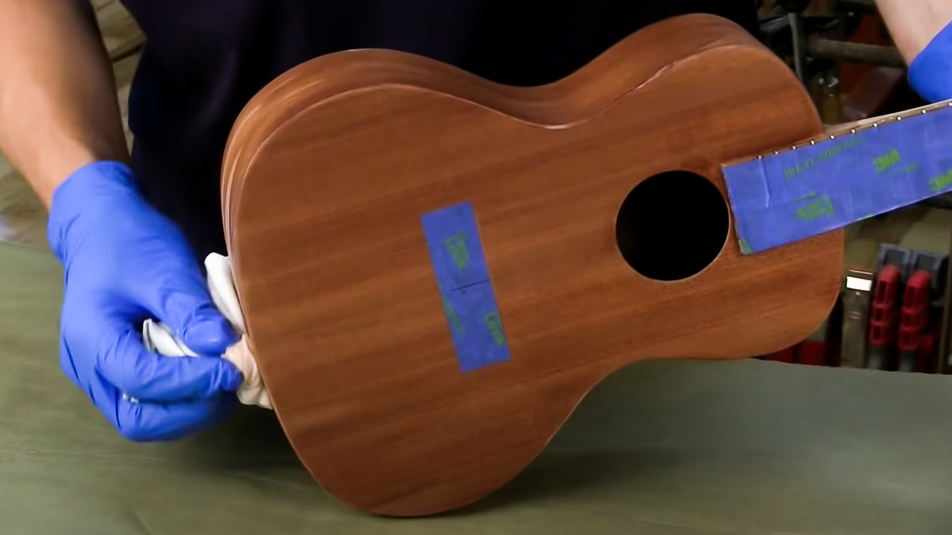 Manos limpiando la capa de acabado del cuerpo del ukulele con un trapo